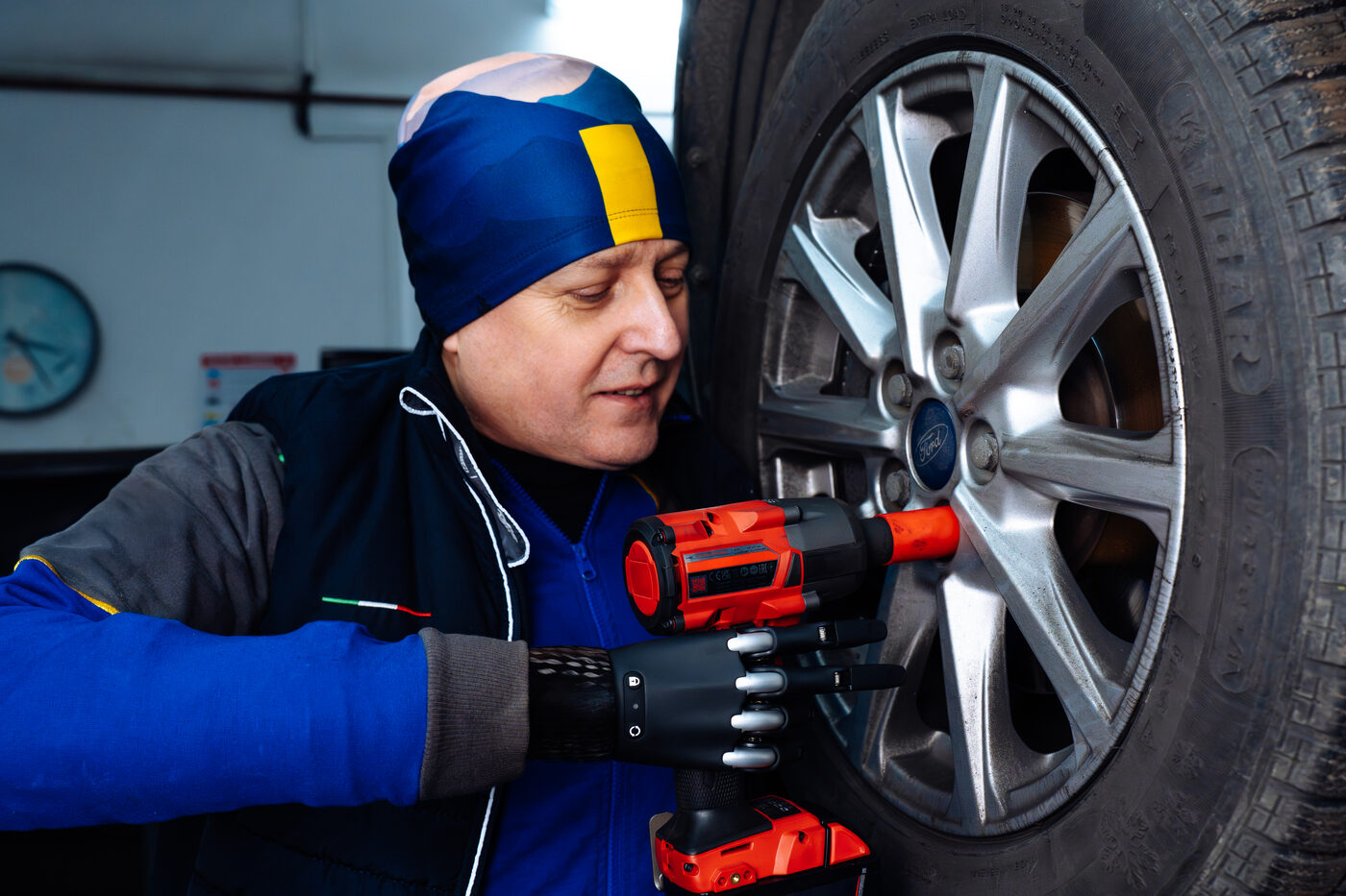 Mechanik z protezą bioniczną Zeus 2 pracuje kluczem udarowym przy kole samochodu